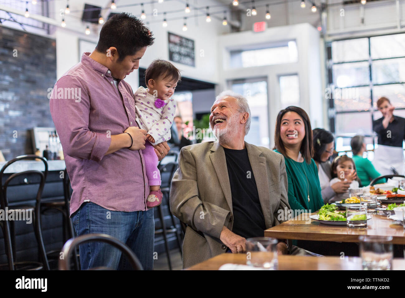 Happy man looking at baby girl being carried by father in restaurant Stock Photo