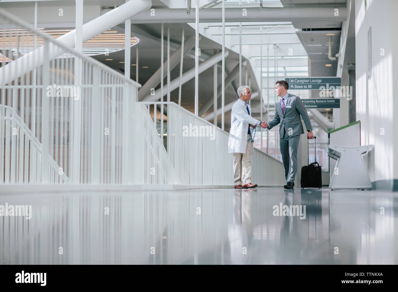 Male doctors shaking hands while walking in hospital corridor Stock Photo