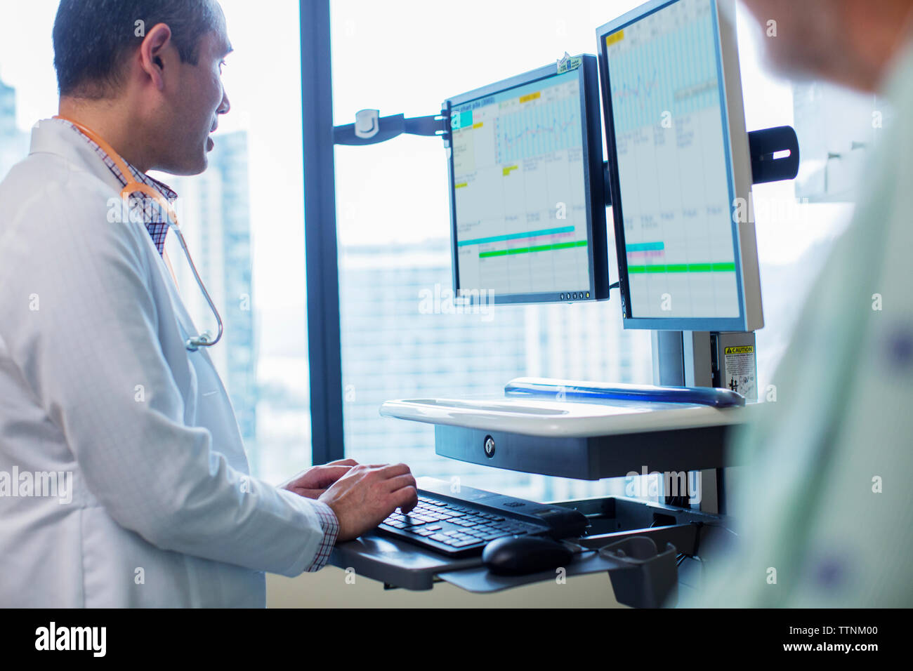 Male doctor using computer while standing by patient in hospital ward