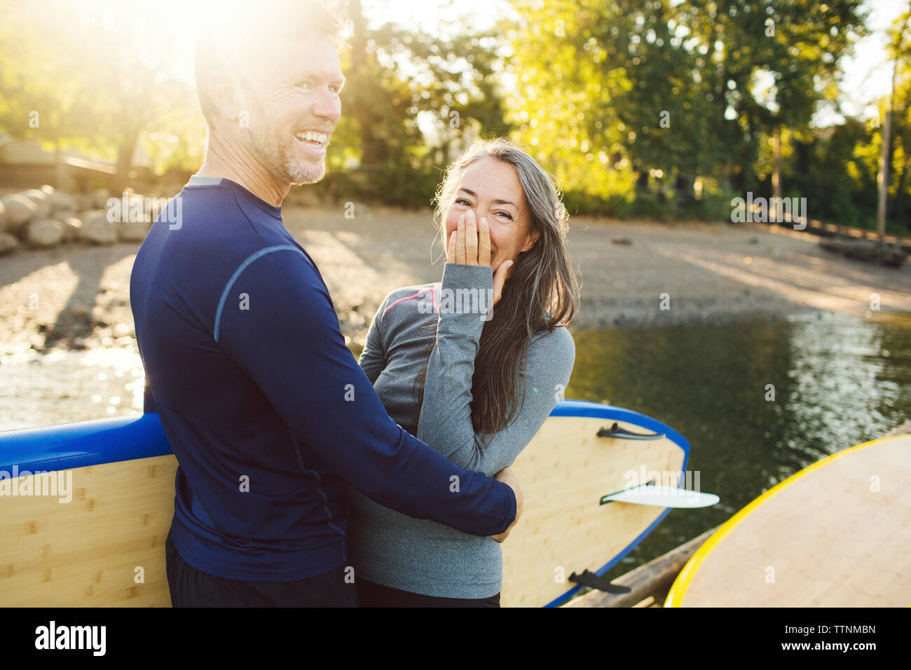 Happy couple with paddleboards standing at riverbank Stock Photo