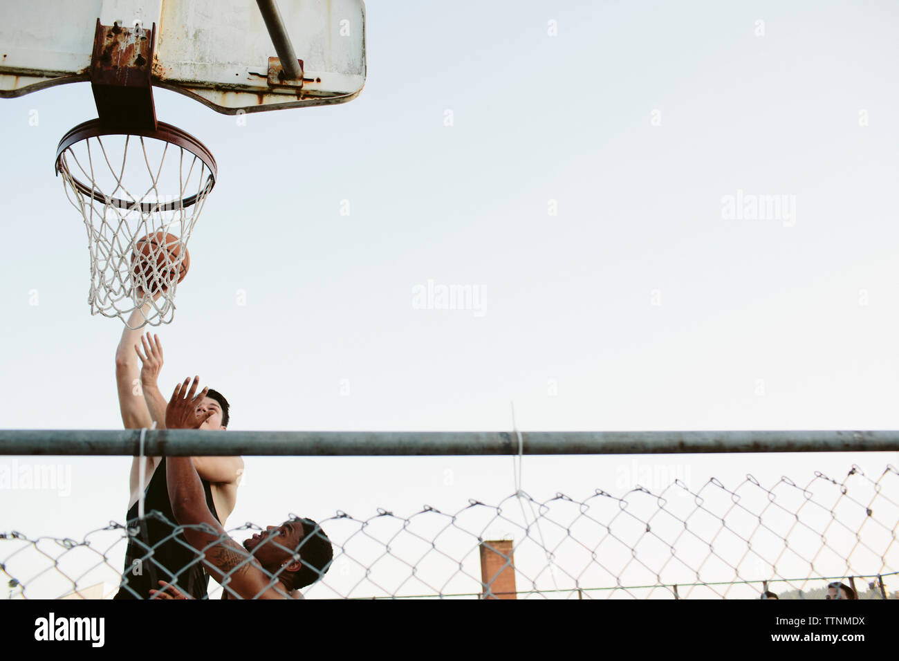 Low angle view of friends playing basketball against clear sky Stock Photo