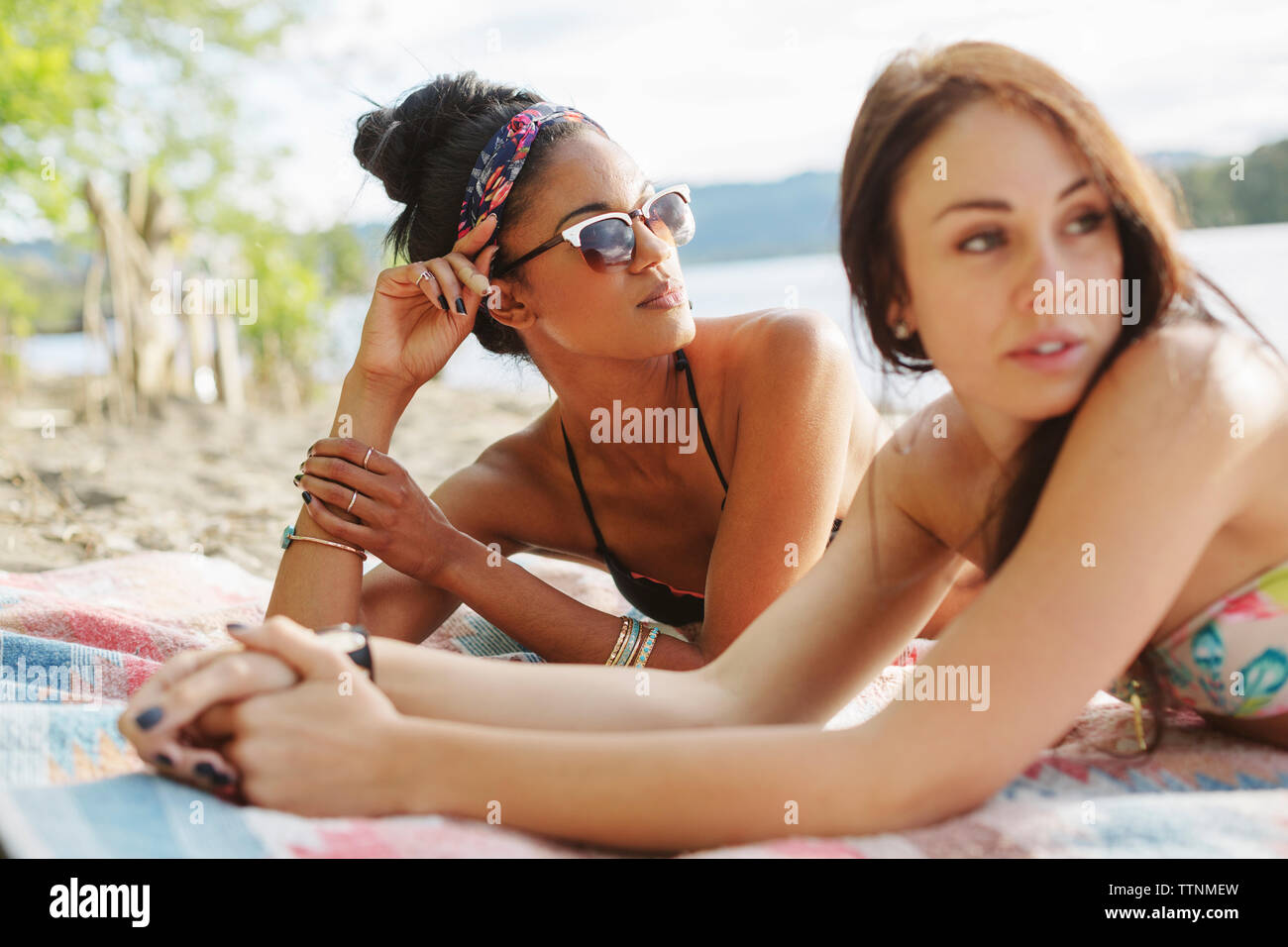 Female friends looking away while lying on picnic blanket at riverbank Stock Photo