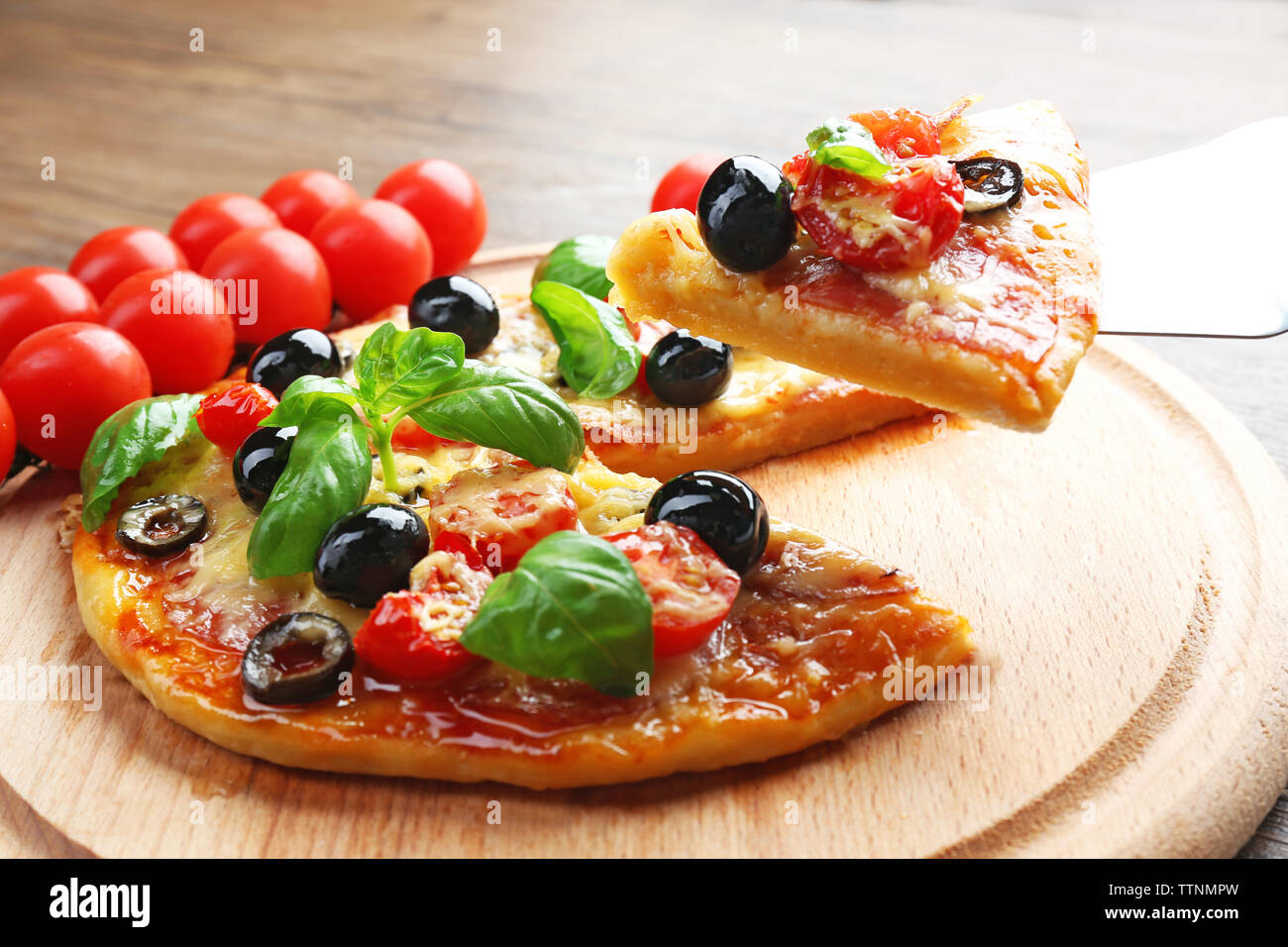Sliced tasty pizza and fresh cherry tomatoes on wooden plate Stock Photo