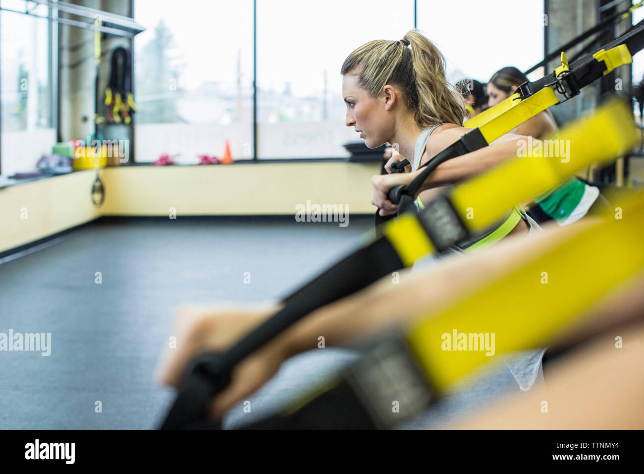 Women pulling resistance bands while exercising in gym Stock Photo