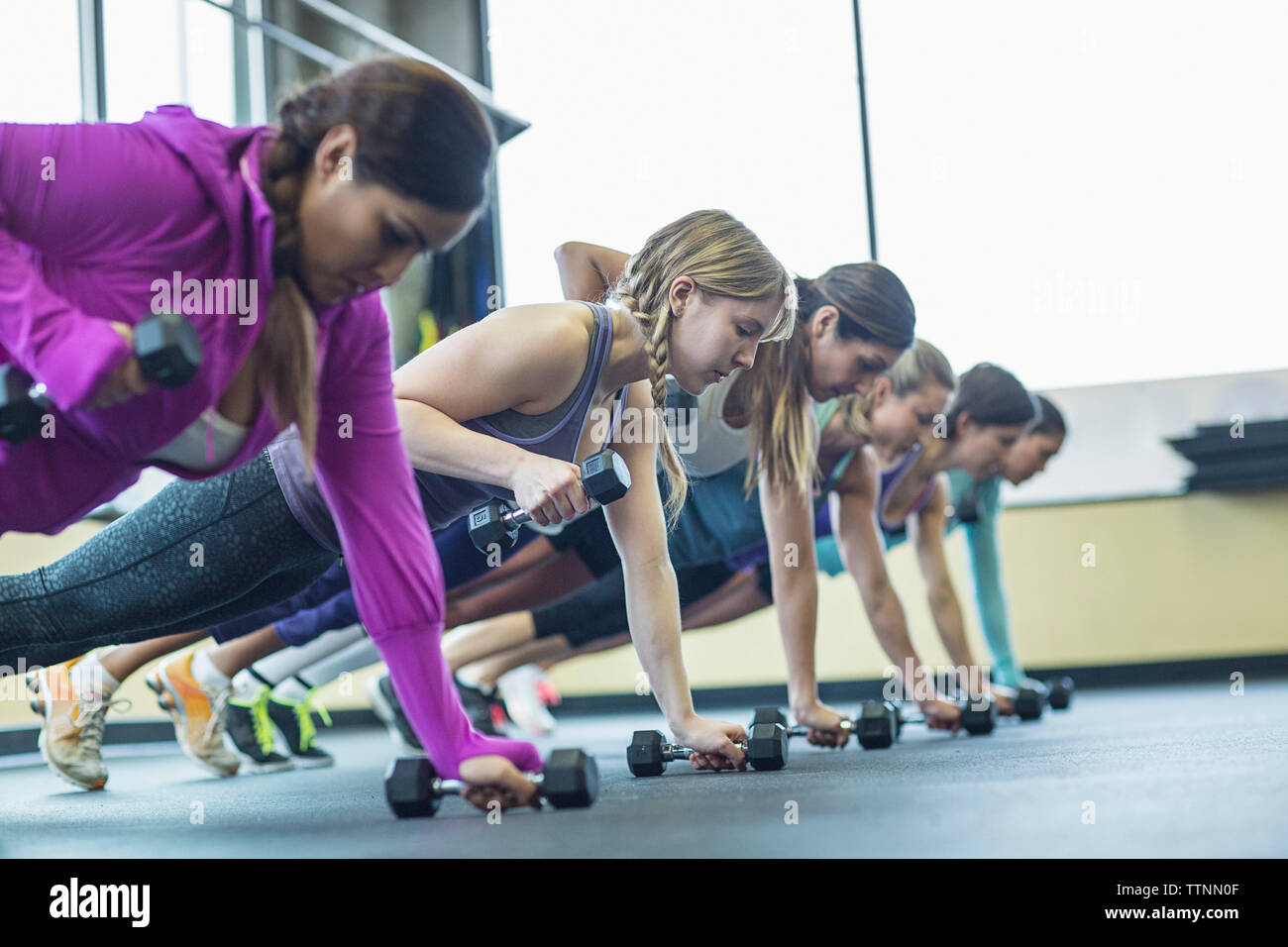 Women doing push-ups with dumbbells at gym Stock Photo