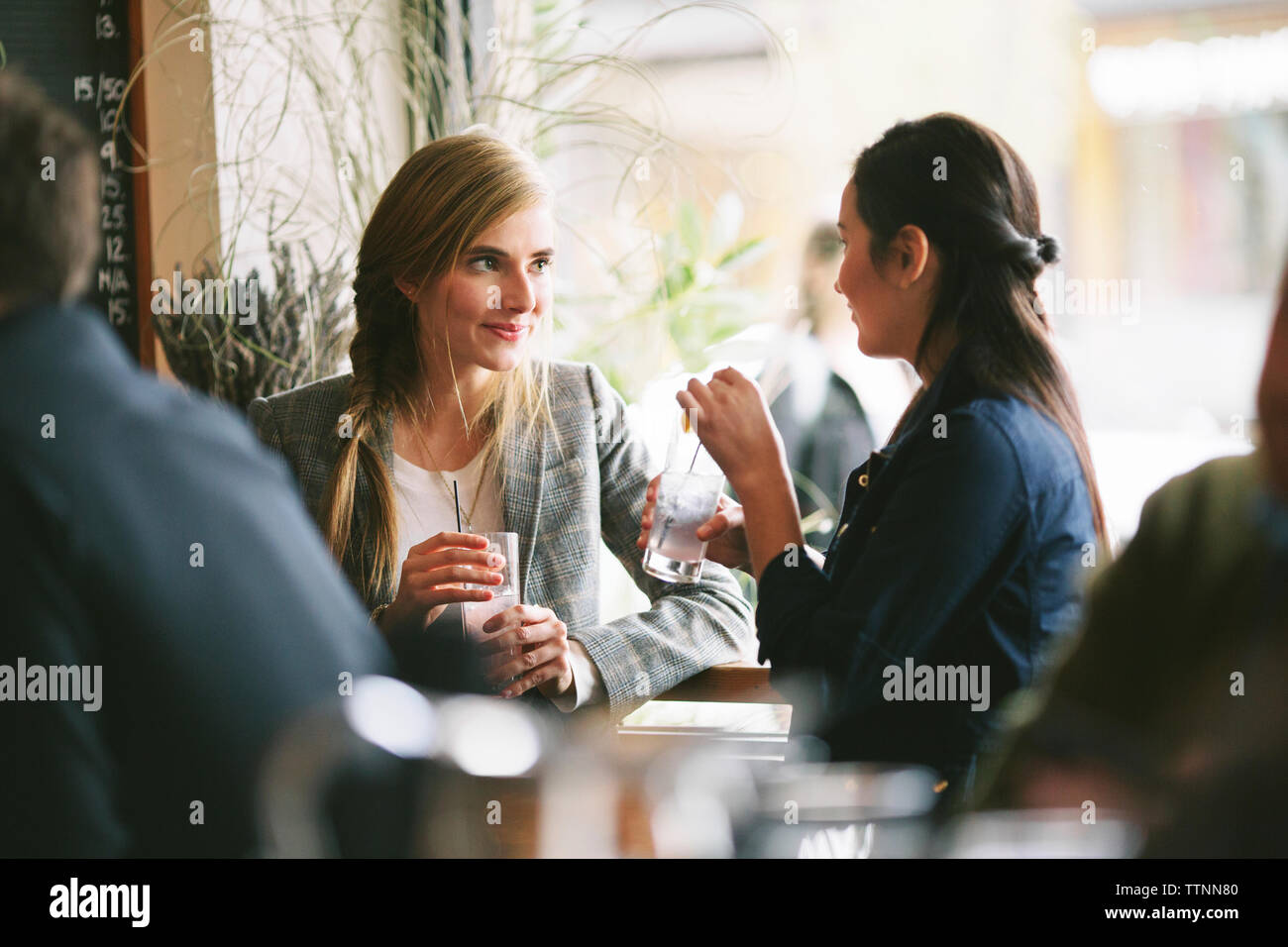 Female friends talking while having drinks by window in restaurant Stock Photo