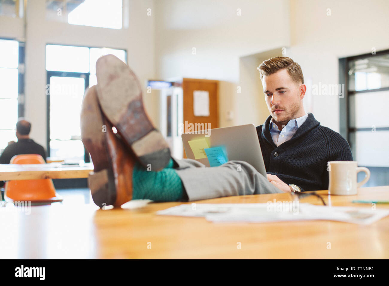 businessman using laptop computer at desk in office while colleague working in background Stock Photo