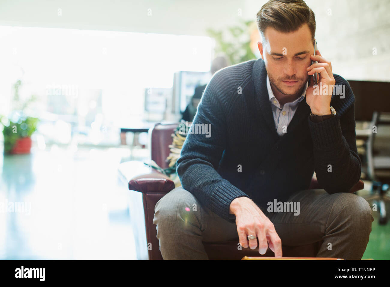 Businessman talking on mobile phone while sitting on chair in office Stock Photo