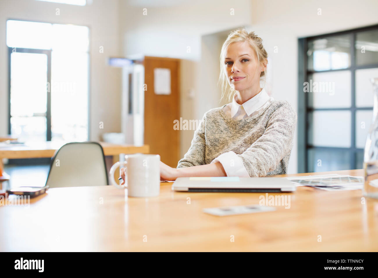 Portrait of confident businesswoman sitting at table with laptop computer in office Stock Photo