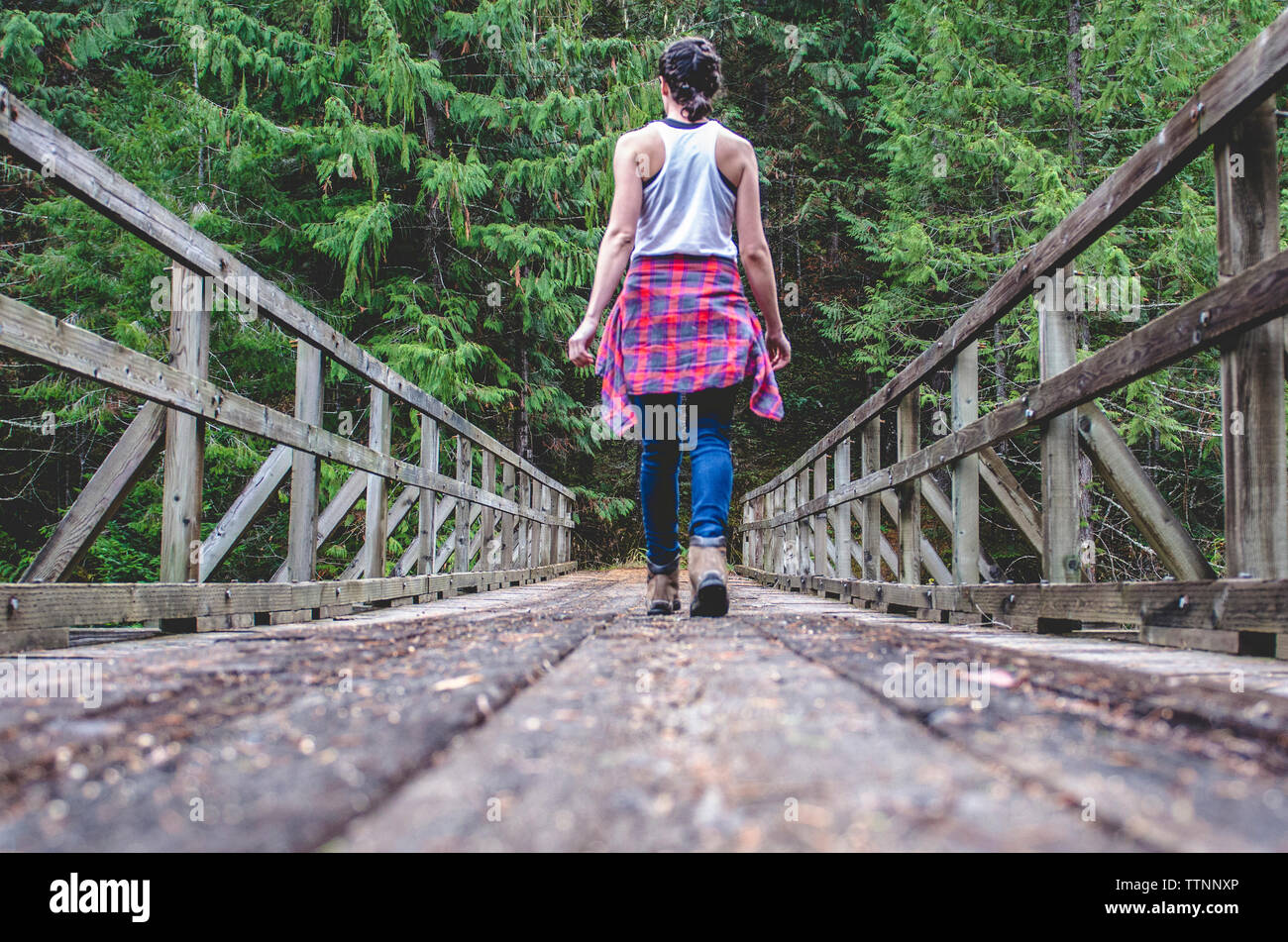 Rear view of woman walking on footbridge amidst trees in forest Stock Photo