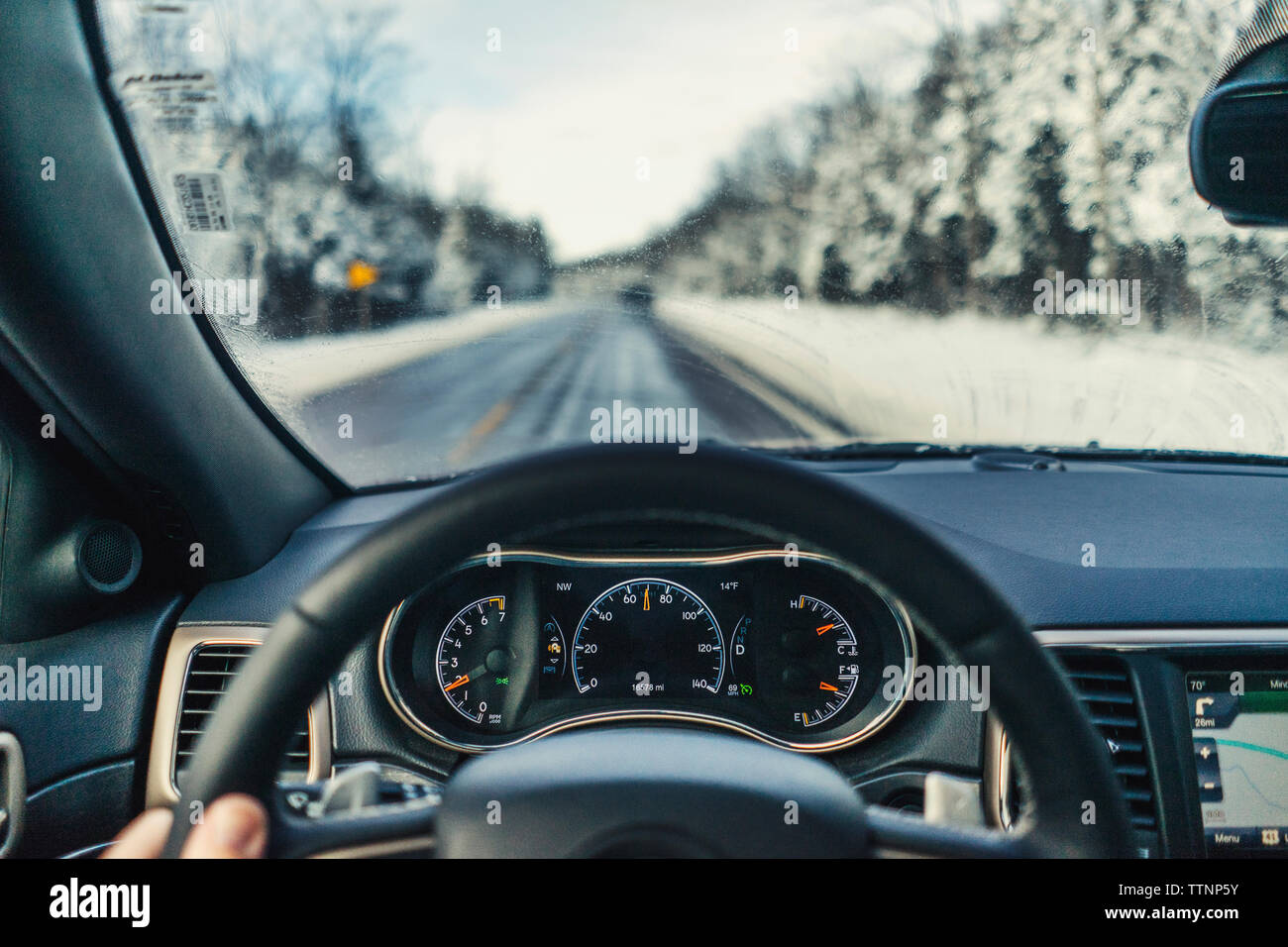 Cropped fingers of man driving car on road during winter Stock Photo