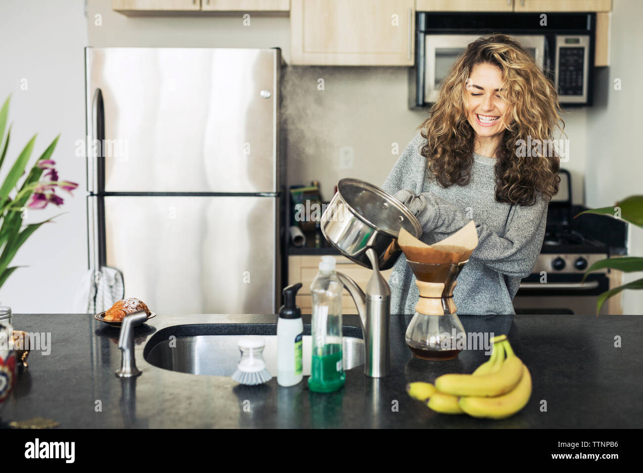 Happy woman pouring coffee in filter at kitchen counter Stock Photo