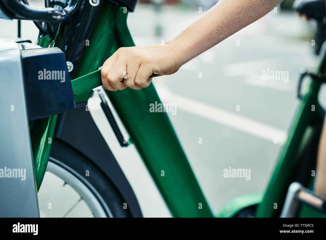 Cropped image of woman unlocking bicycle from rack at street Stock Photo