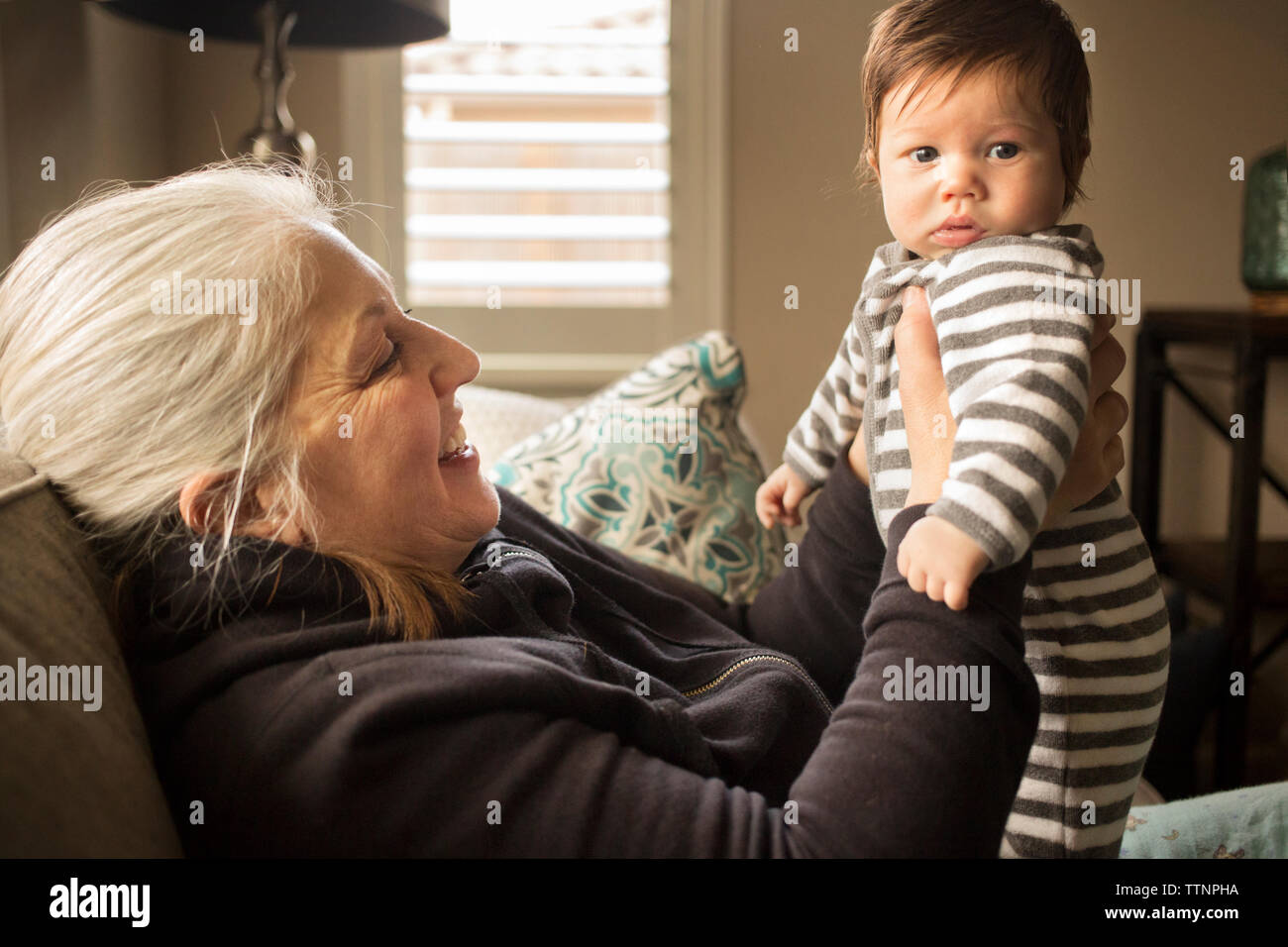 Grandmother holding baby grandson on sofa at home Stock Photo
