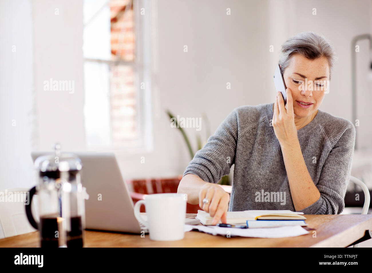 Mature woman communicating on phone while working at table Stock Photo