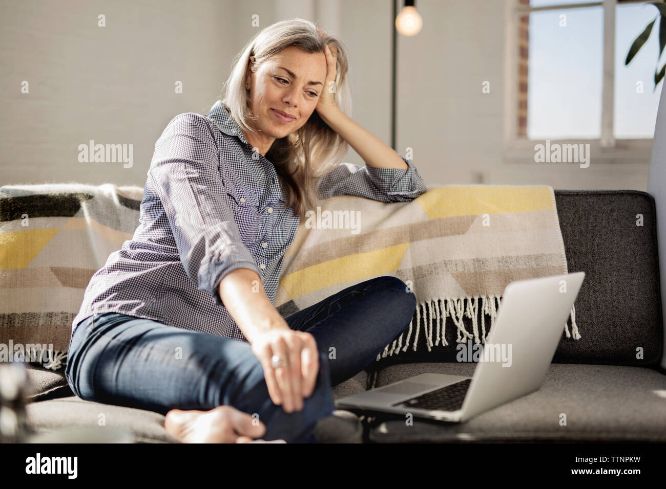 Relaxed woman with laptop sitting on sofa Stock Photo