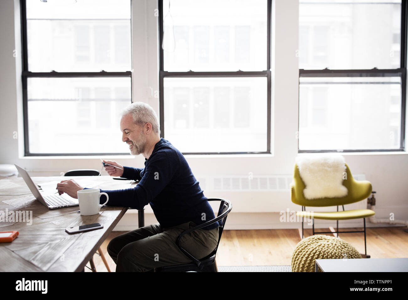 Side view of man using laptop computer while sitting at home Stock Photo