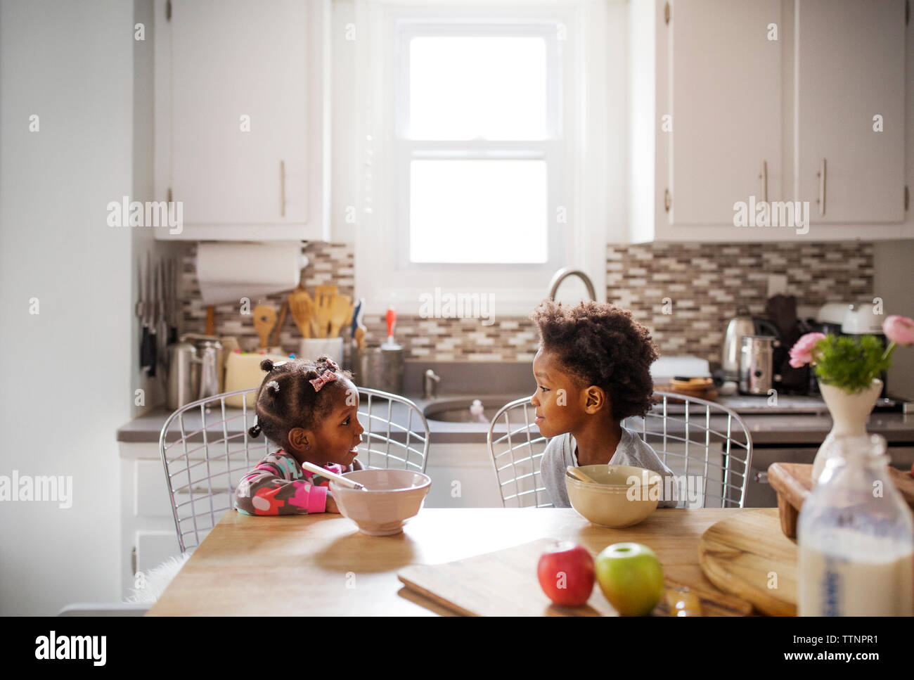 Brother and sister talking while having breakfast in kitchen Stock Photo