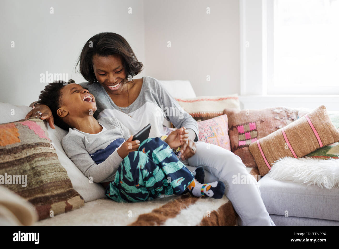 Boy laughing while using tablet computer with mother on sofa at home Stock Photo