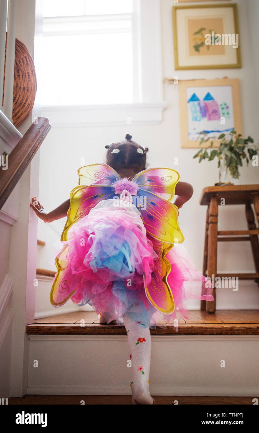 Rear view of girl in fairy costume moving up steps at home Stock Photo ...