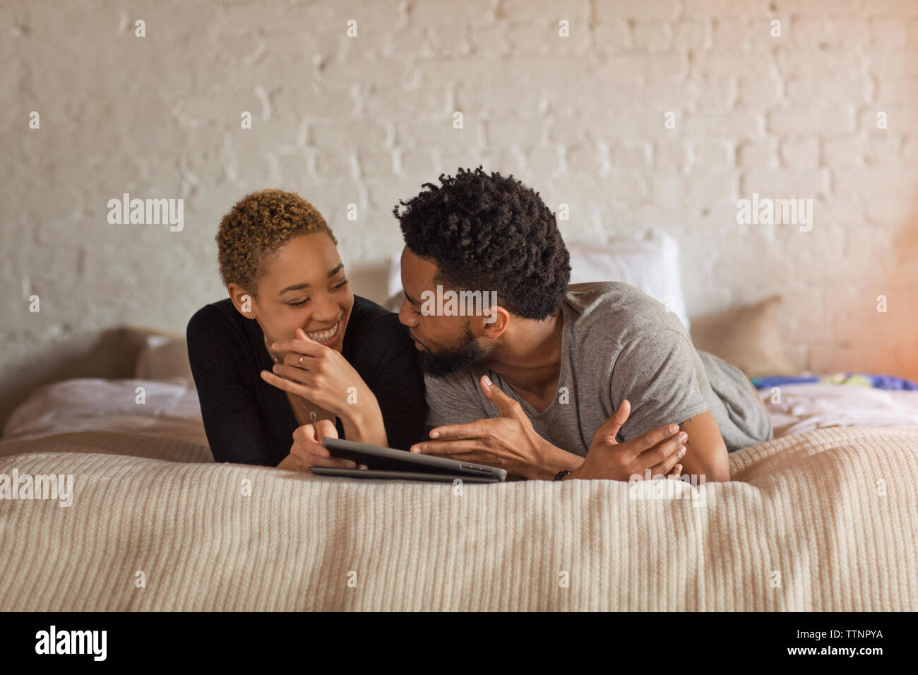 Happy couple talking while using tablet computer on bed at home Stock Photo