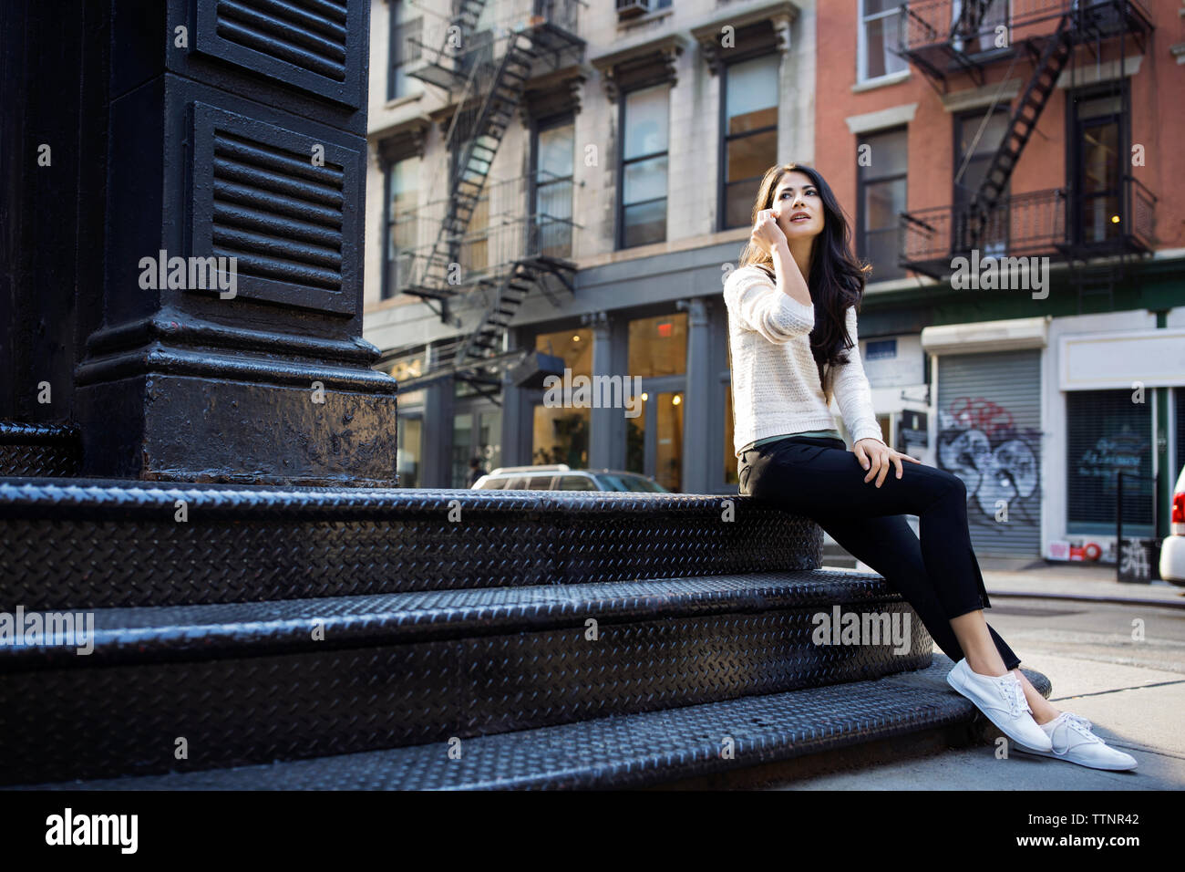 Young woman answering smart phone while sitting on steps outdoors Stock Photo
