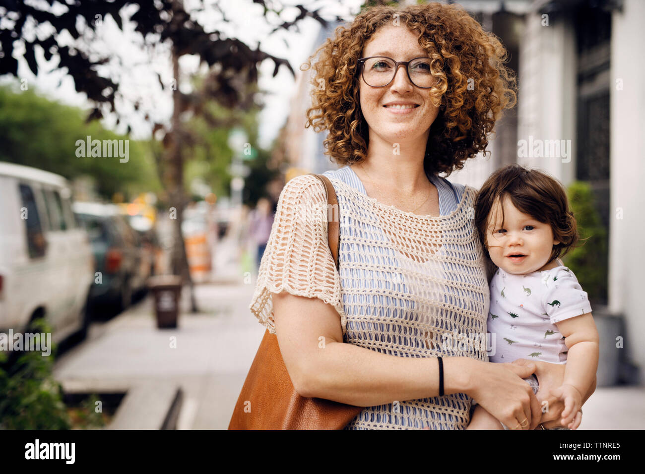 Portrait of smiling mother carrying baby boy while standing on footpath Stock Photo