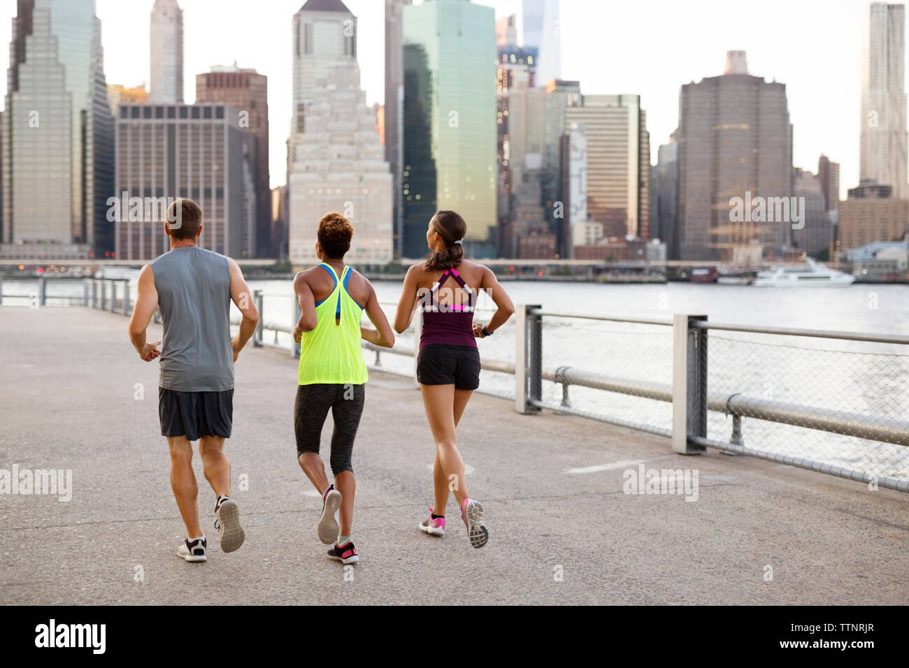 Athletes jogging on promenade by river Stock Photo