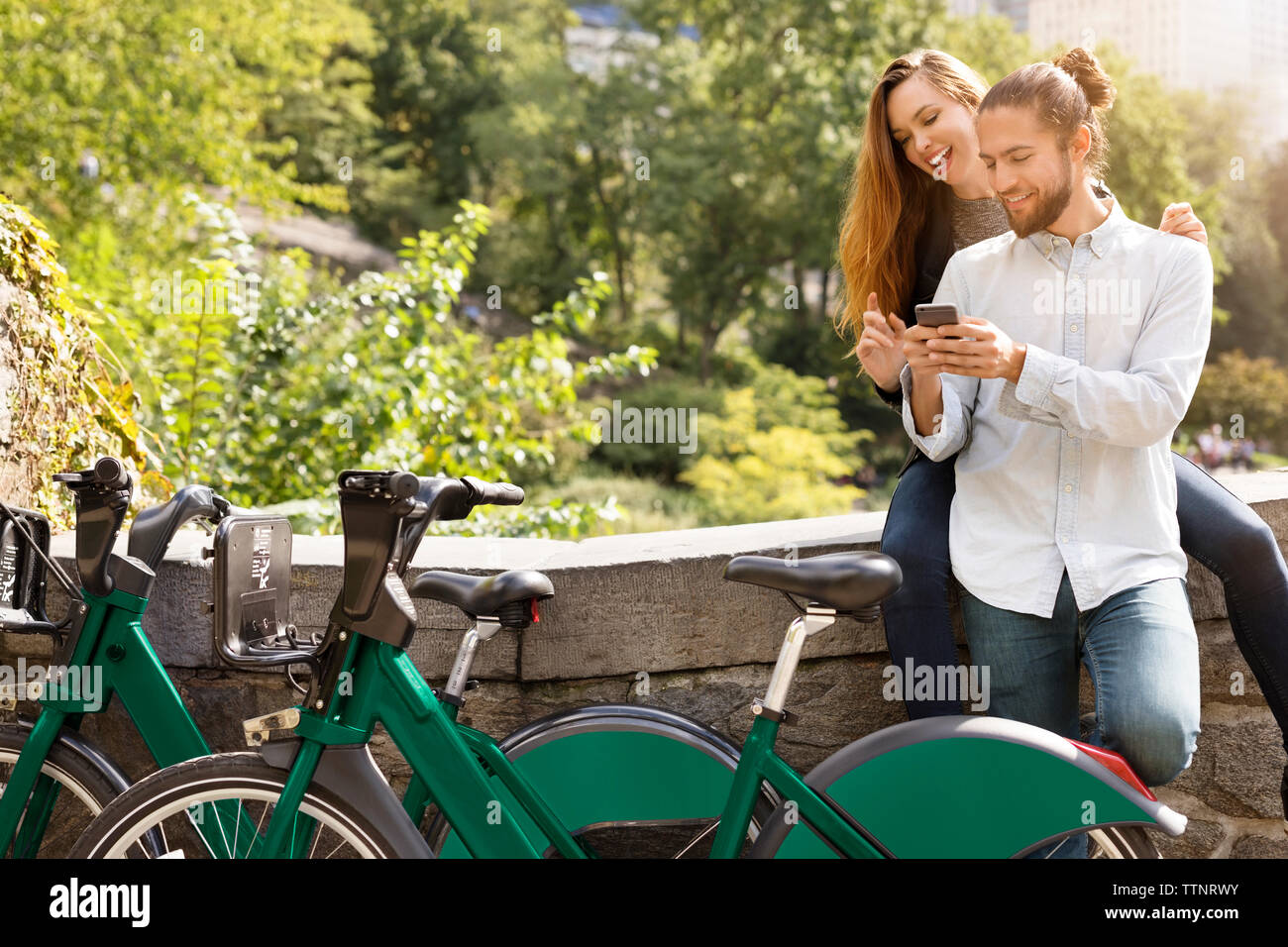 Couple using mobile phone while leaning on retaining wall Stock Photo