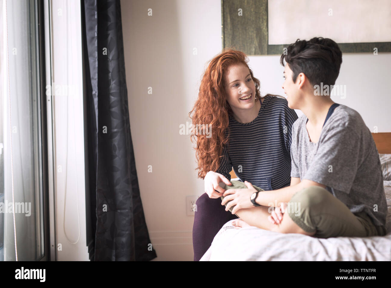 Happy couple talking while sitting on bed at home Stock Photo