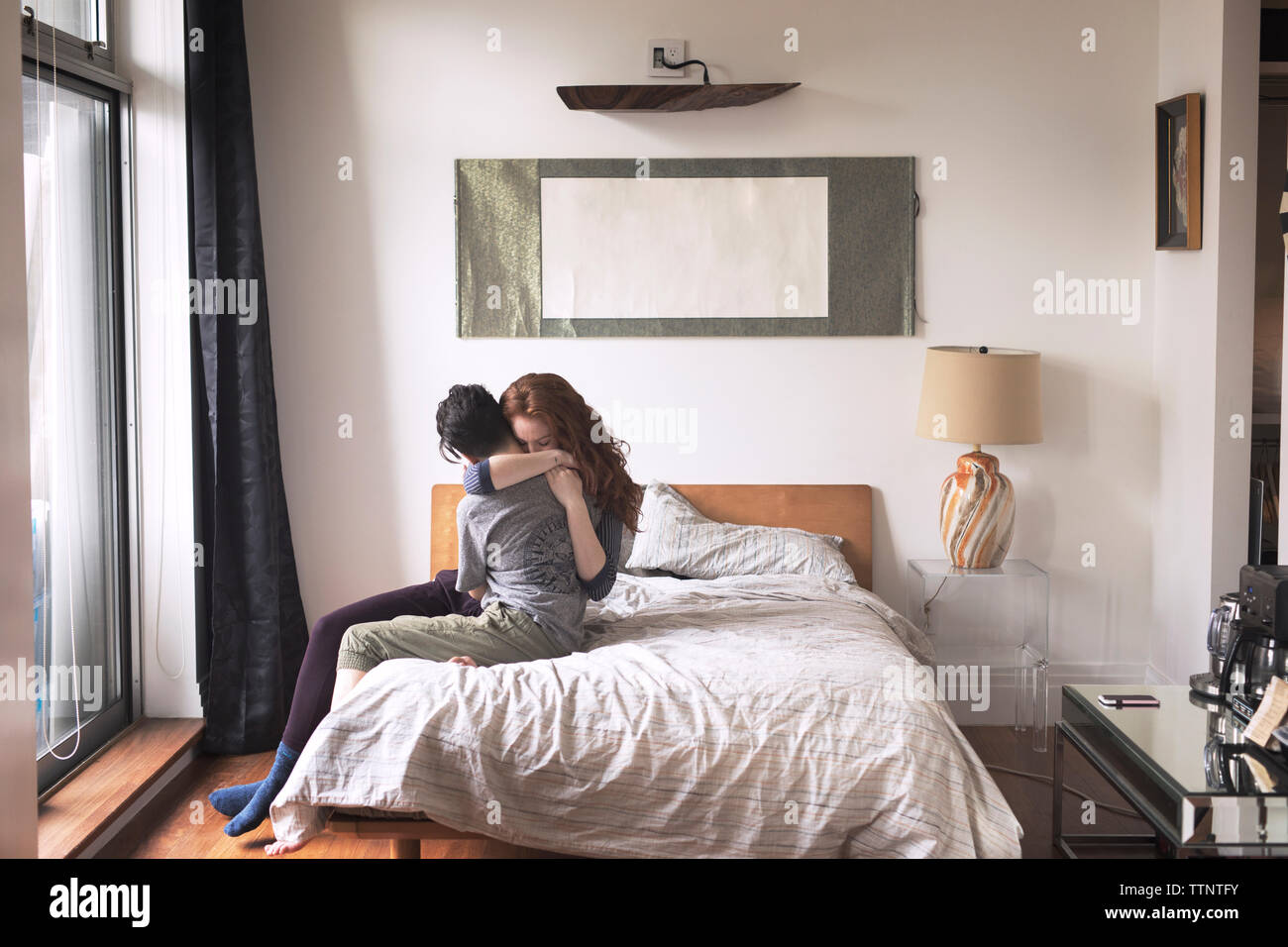 Lesbians embracing while sitting on bed at home Stock Photo