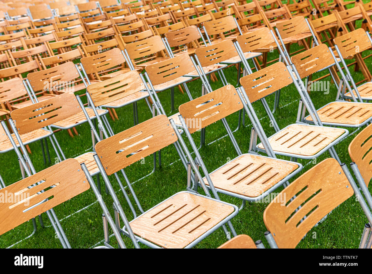 Lot of wooden chairs stand outside in the park in the rain. Empty