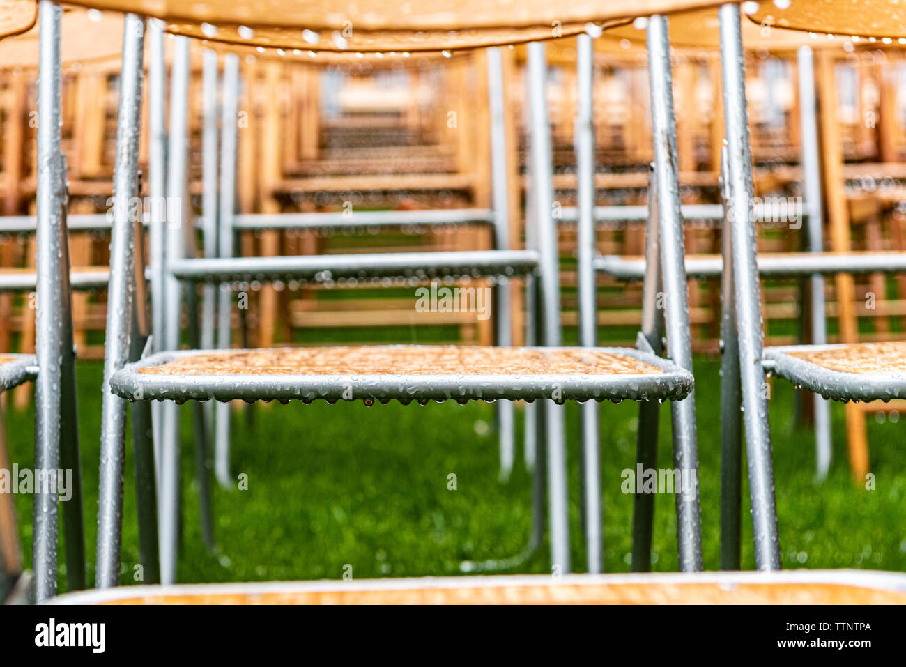 Lot of wooden chairs stand outside in the park in the rain. Empty