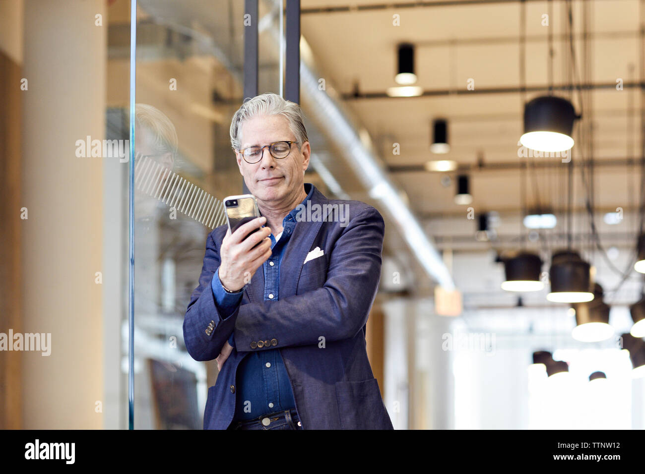 businessman looking at smart phone while standing by door in office Stock Photo