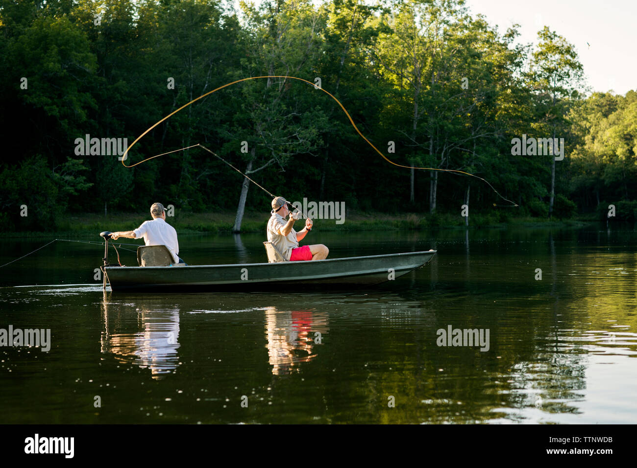 Man casting fishing line in lake with friend sitting in rowboat Stock Photo