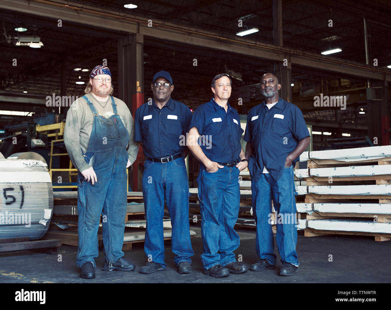 Full length portrait of coworkers standing against manufacturing objects in industry Stock Photo