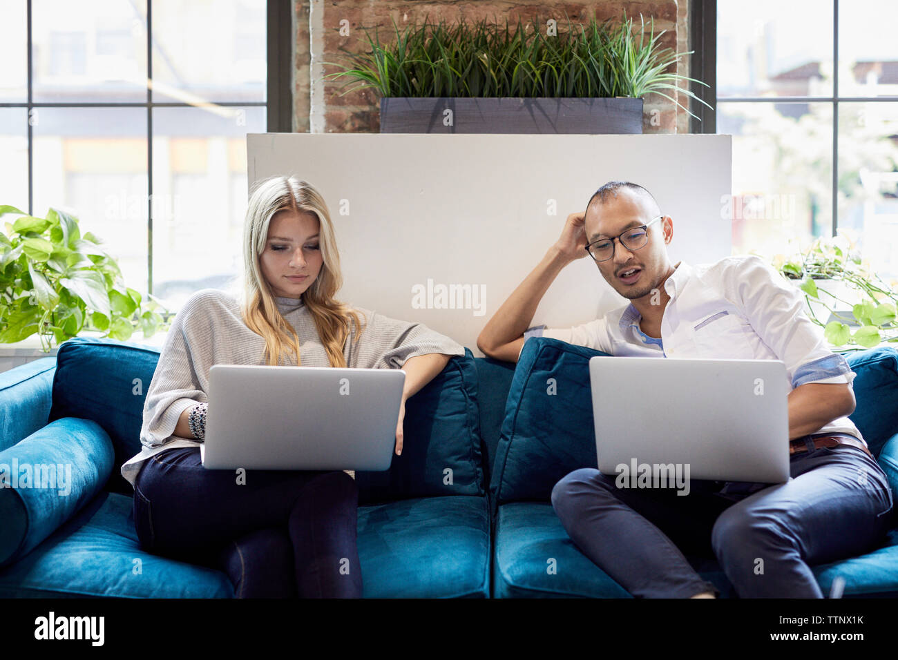 Young business people using laptops while sitting on sofa at creative office Stock Photo