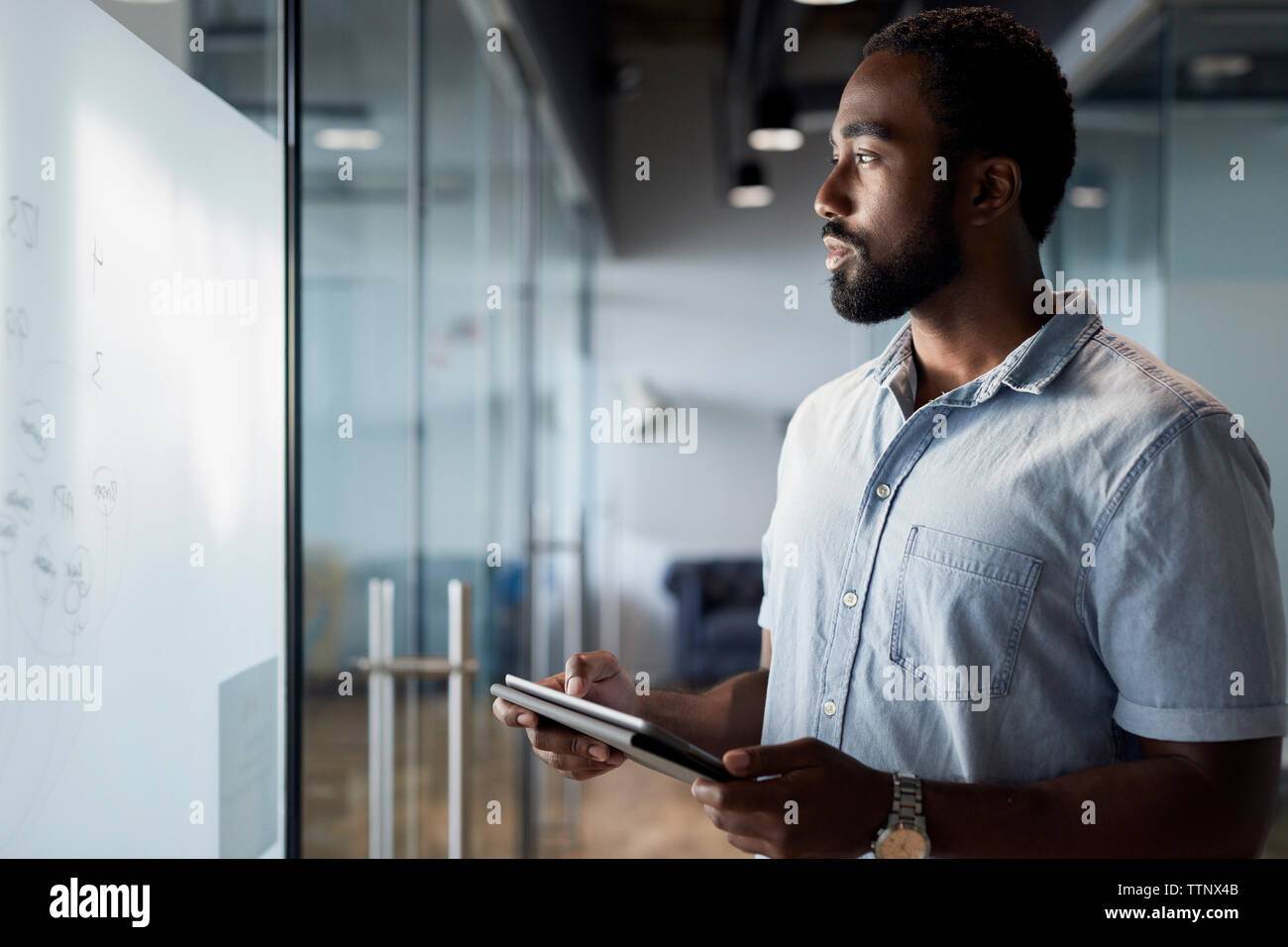 Thoughtful businessman using digital tablet while standing at office corridor Stock Photo