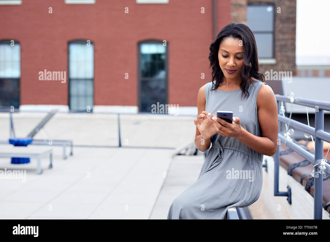 businesswoman using smart phone while sitting railing at building terrace Stock Photo