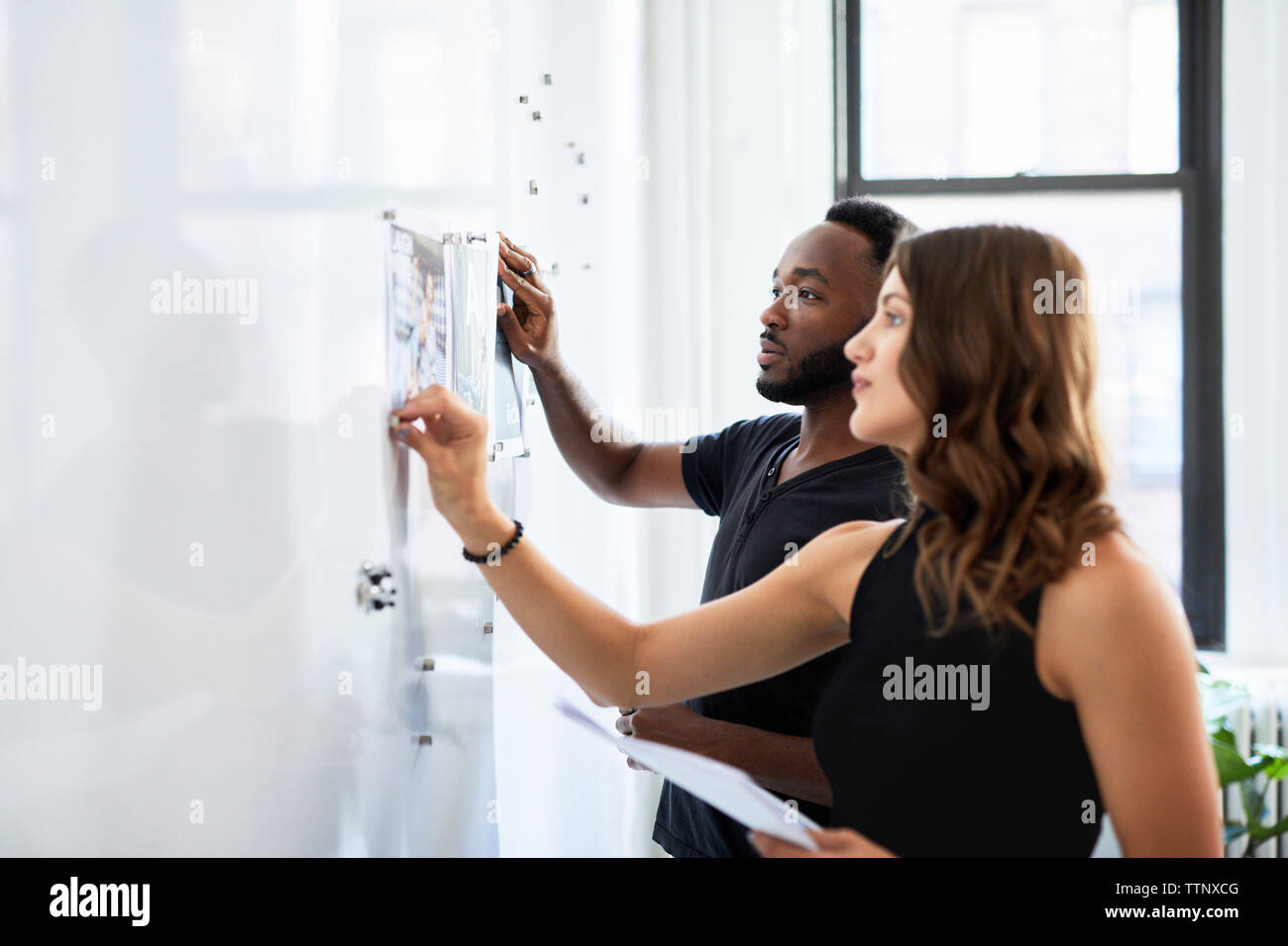 Serious business colleagues looking at photograph printouts attached on bulletin board in office Stock Photo