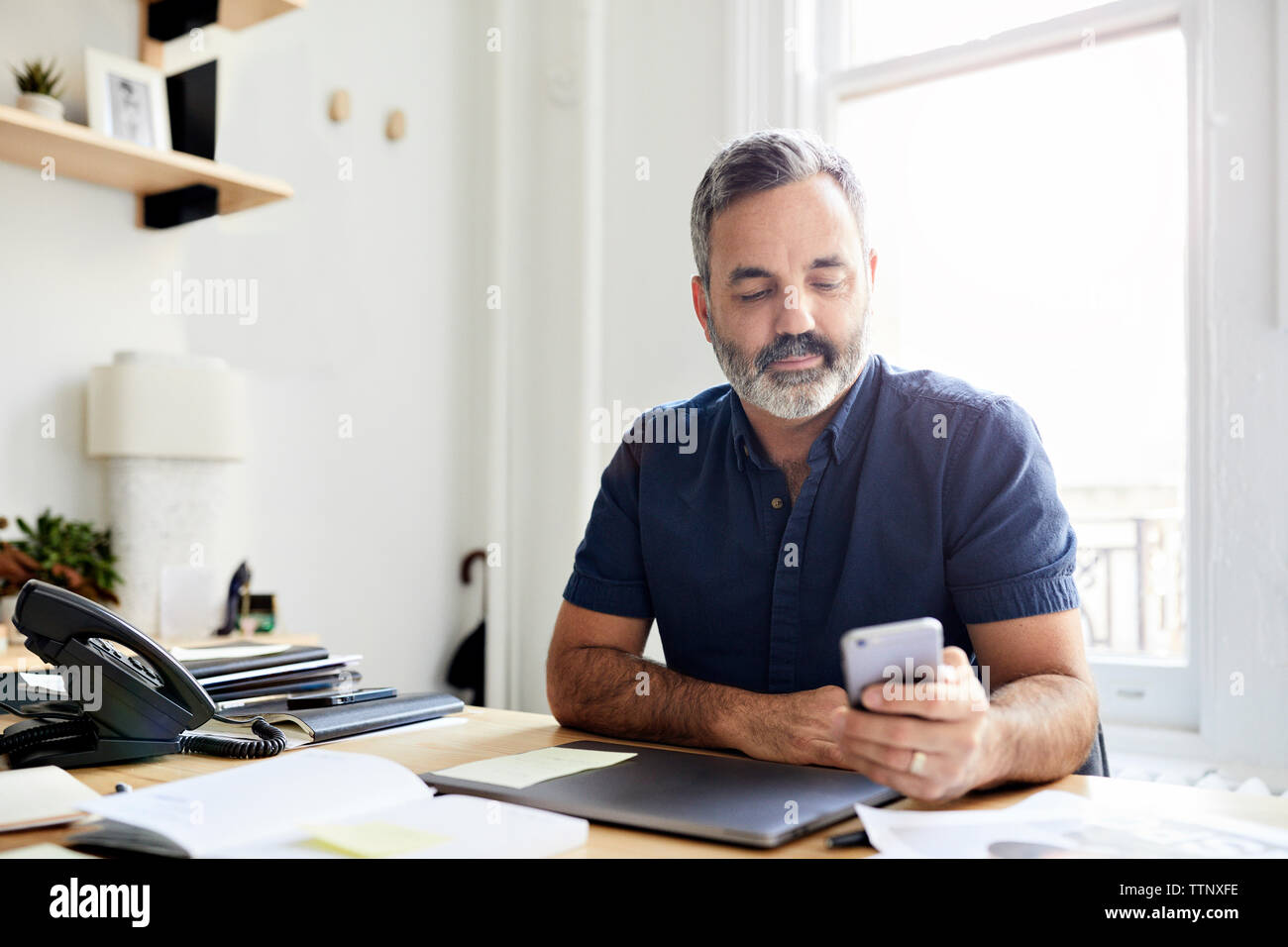 businessman using smart phone while sitting at desk in creative office Stock Photo