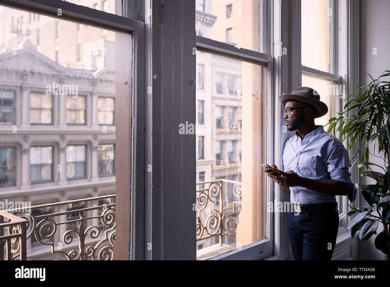 businessman using mobile phone while standing by window in creative office Stock Photo