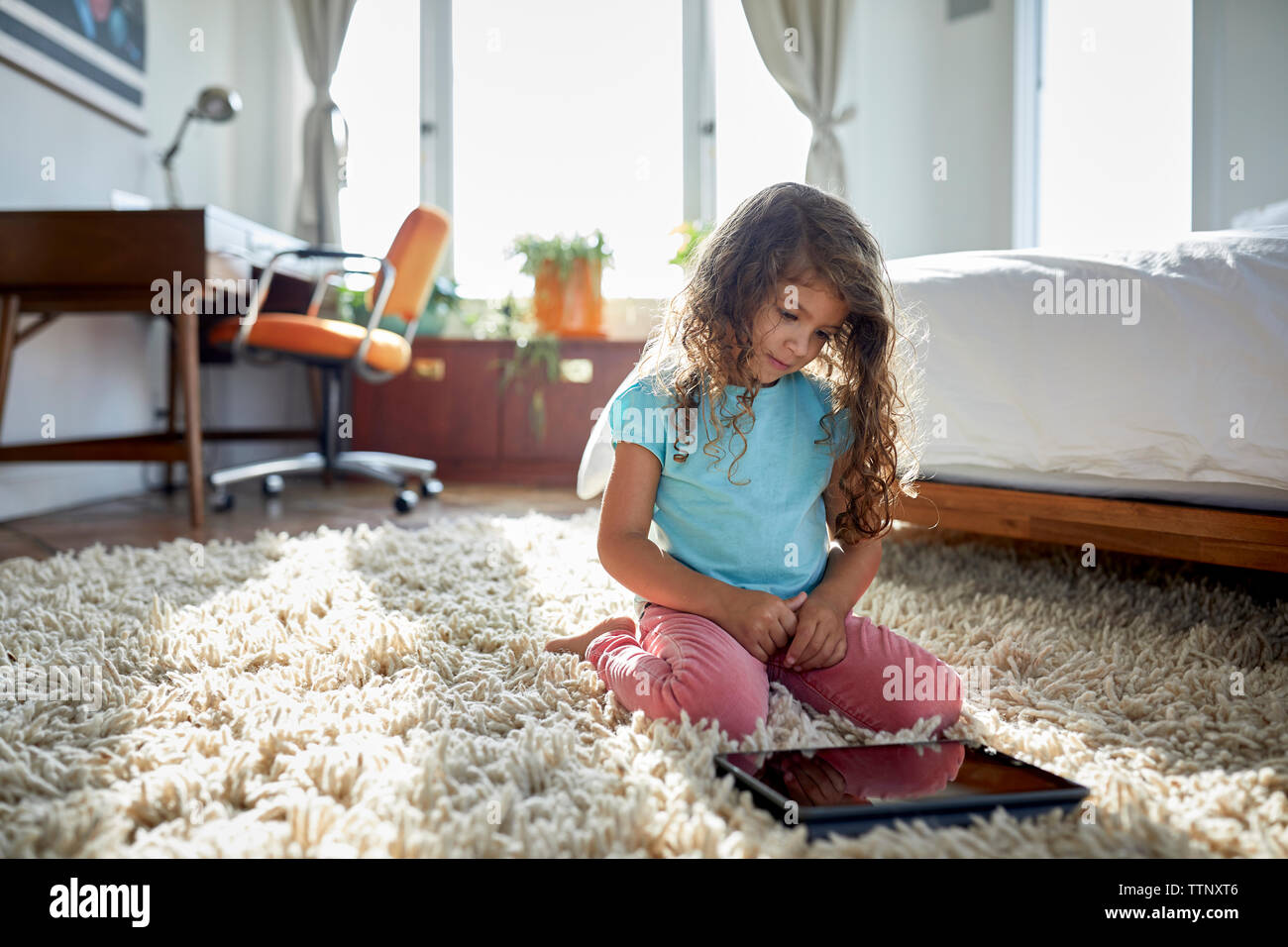 Girl using tablet computer while kneeling on rug in bedroom Stock Photo ...