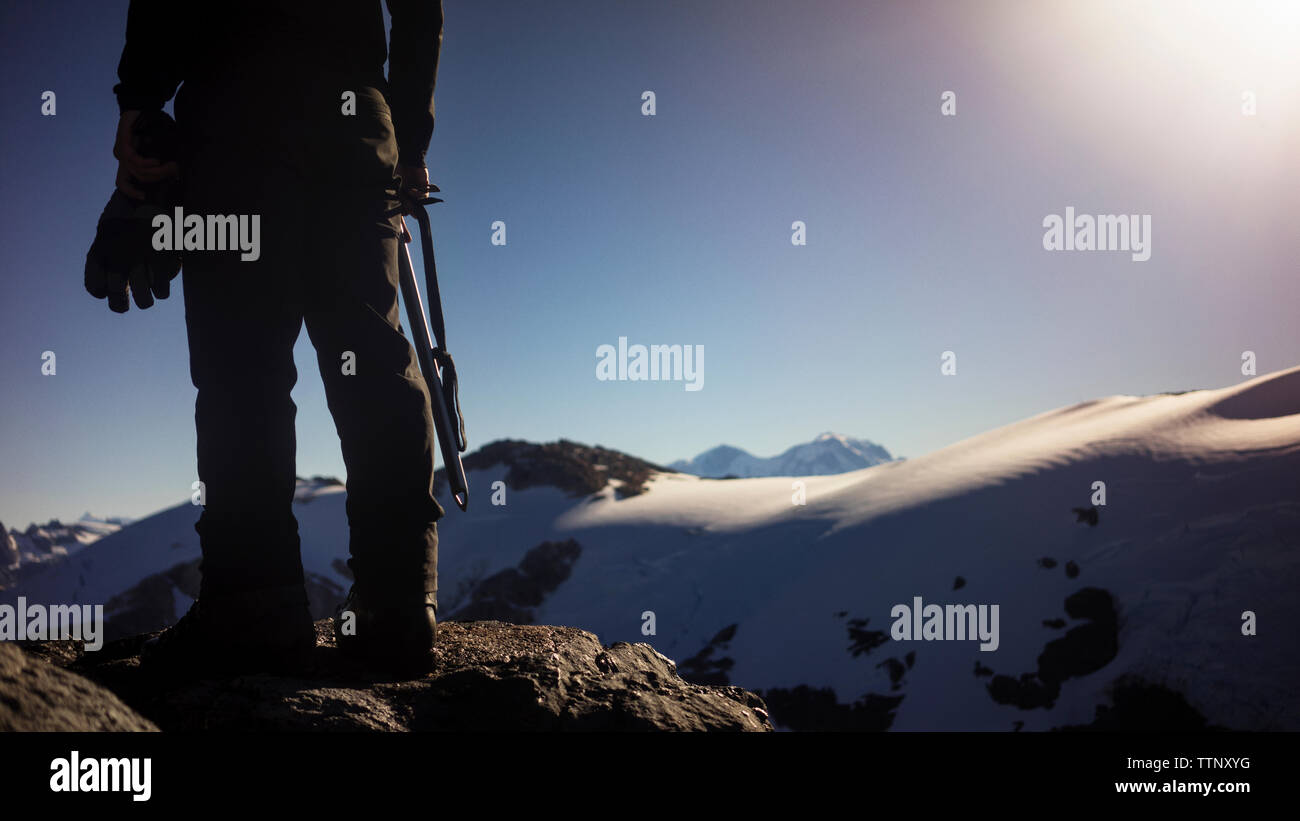 Low section of man standing on rock against mountains and clear sky Stock Photo