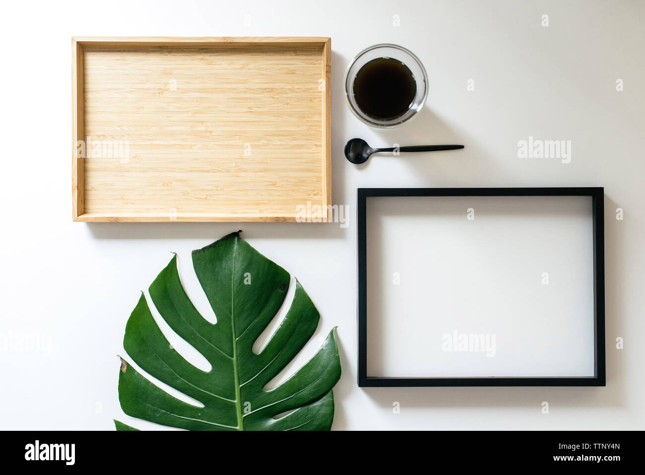 Overhead view of coffee with picture frame by monstera leaf by wooden tray arranged on white background Stock Photo