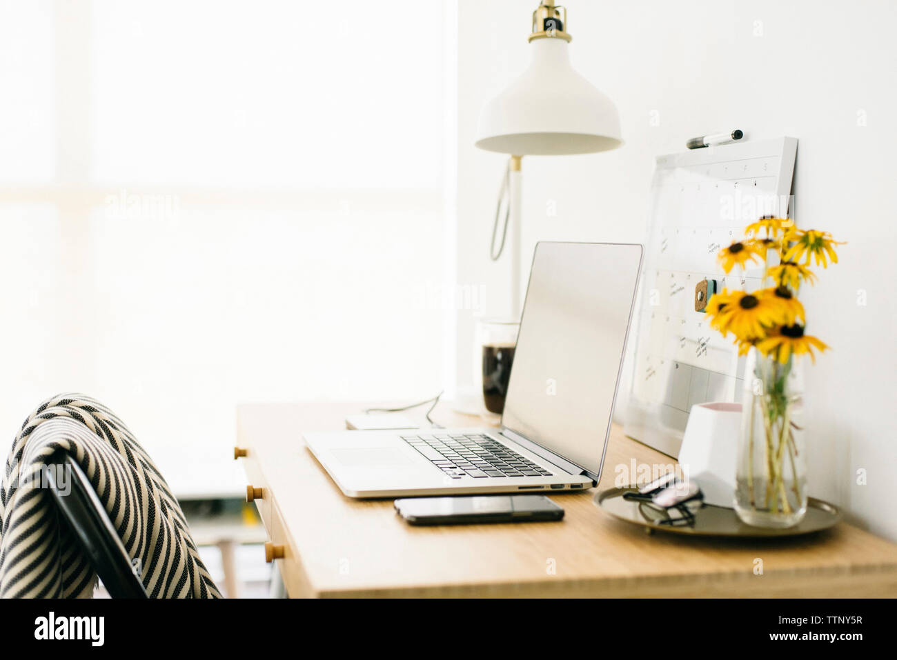 Technologies with calendar and flower vase by desk lamp on wooden table in office Stock Photo
