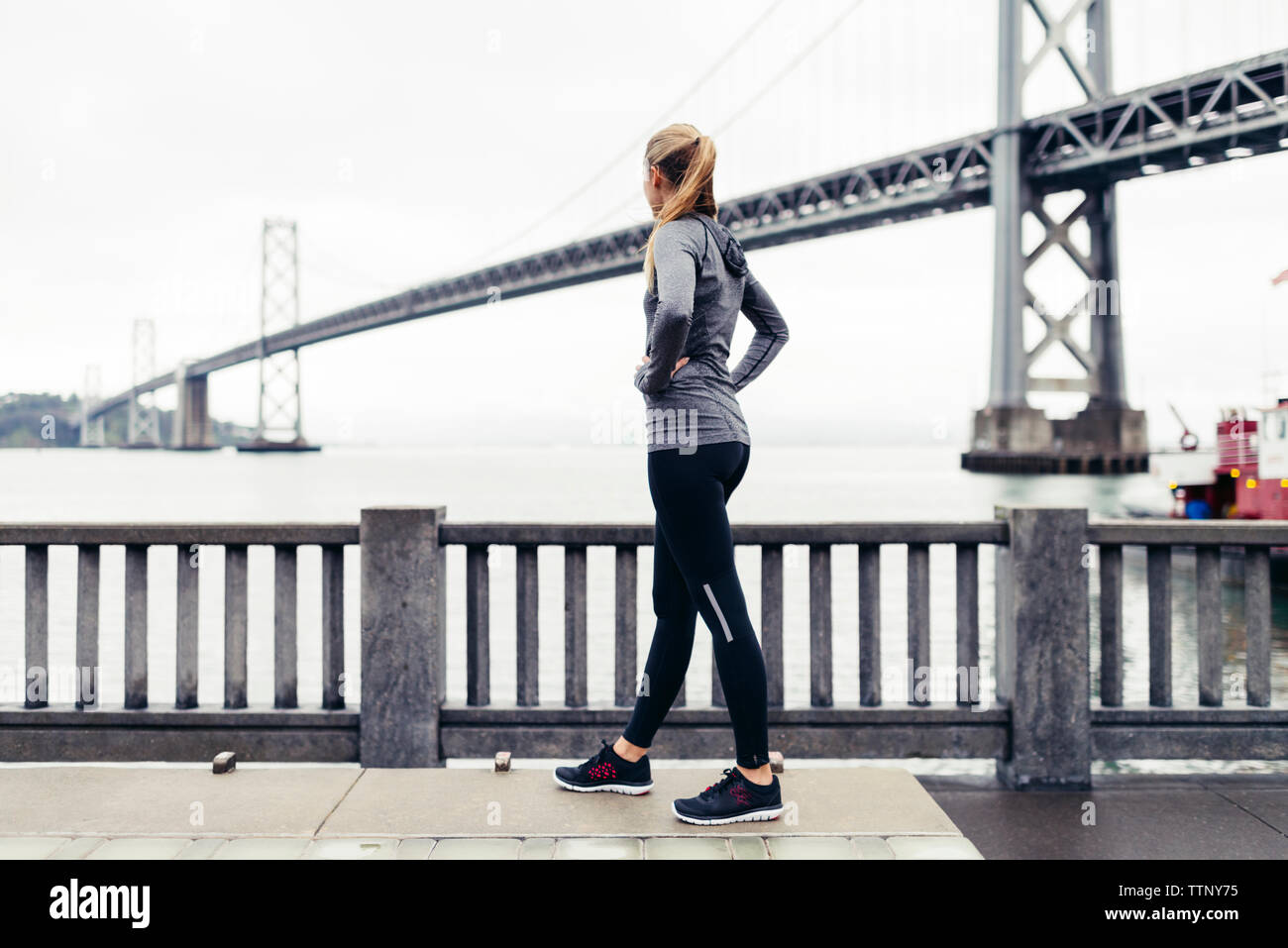 Side view of female athlete looking at Oakland Bay Bridge while standing on footpath Stock Photo