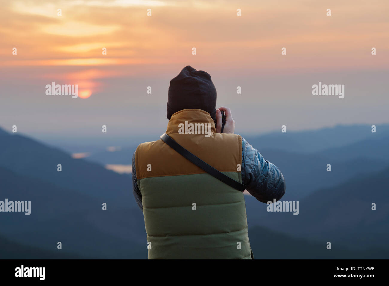 Rear view of male hiker photographing mountains during sunset Stock Photo