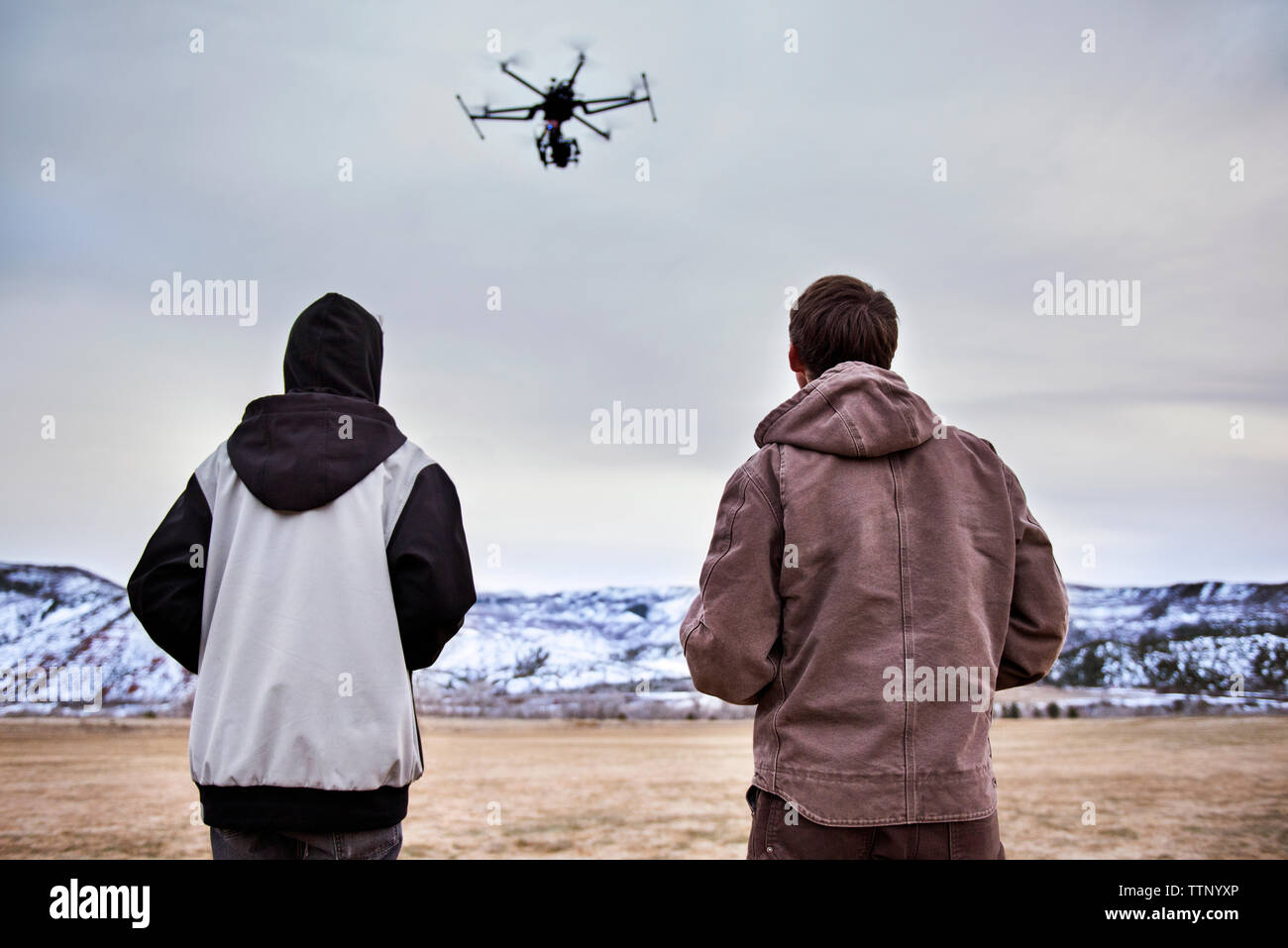 Rear view of father and son flying Drone over field during winter Stock Photo