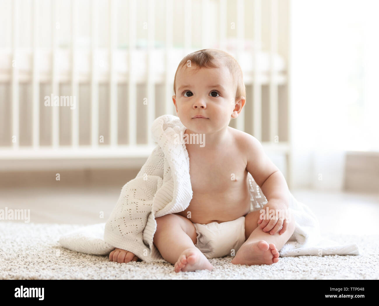 Cute baby sitting beside his bed on the floor Stock Photo Alamy
